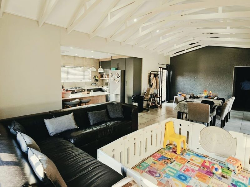 Spacious open-plan living and dining area featuring a vaulted ceiling with exposed trusses, tiled floors, and a modern kitchen with a central island.
