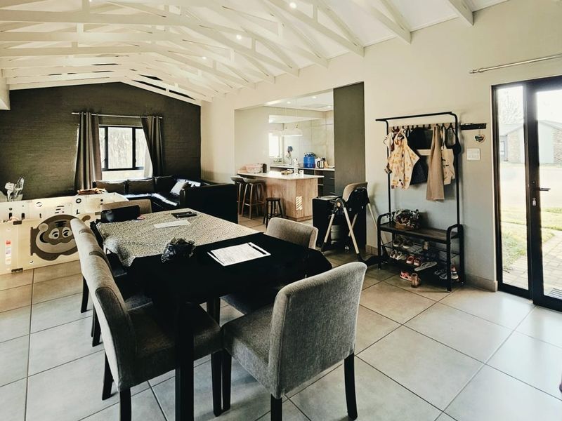 Spacious open-plan living and dining area featuring exposed timber rafters, tiled flooring, and seamless flow to the kitchen and outdoor access.