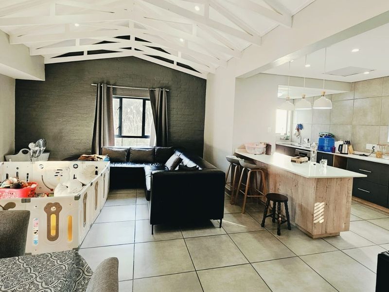 Spacious open-plan living and kitchen area featuring exposed white roof trusses, modern cabinetry, a central island, and large format floor tiles.