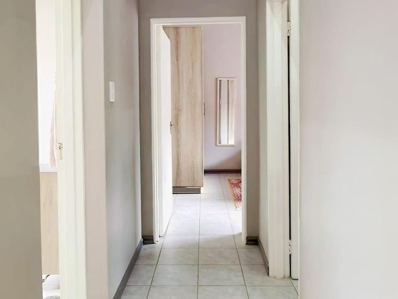 A clean, neutral-toned hallway featuring tiled flooring and access to adjacent rooms with built-in storage visible in the distance.