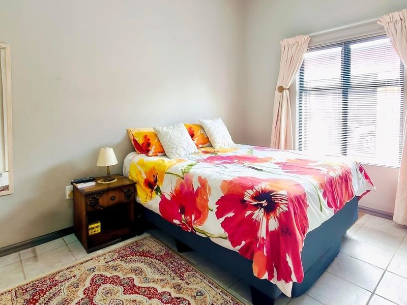 A functional bedroom featuring tiled flooring, neutral wall finishes, and a window with fitted blinds and curtains.