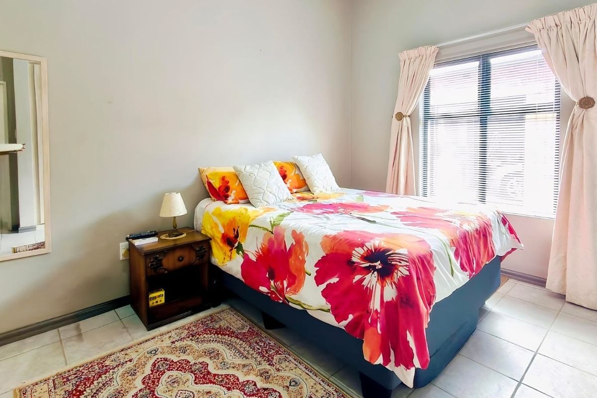 A functional bedroom featuring tiled flooring, neutral wall finishes, and a window with fitted blinds and curtains.