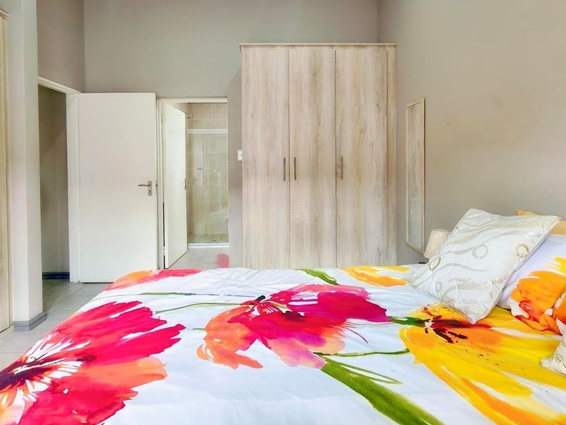 A well-maintained bedroom featuring light wood-finish built-in cupboards, tiled flooring, and direct access to an en-suite bathroom.