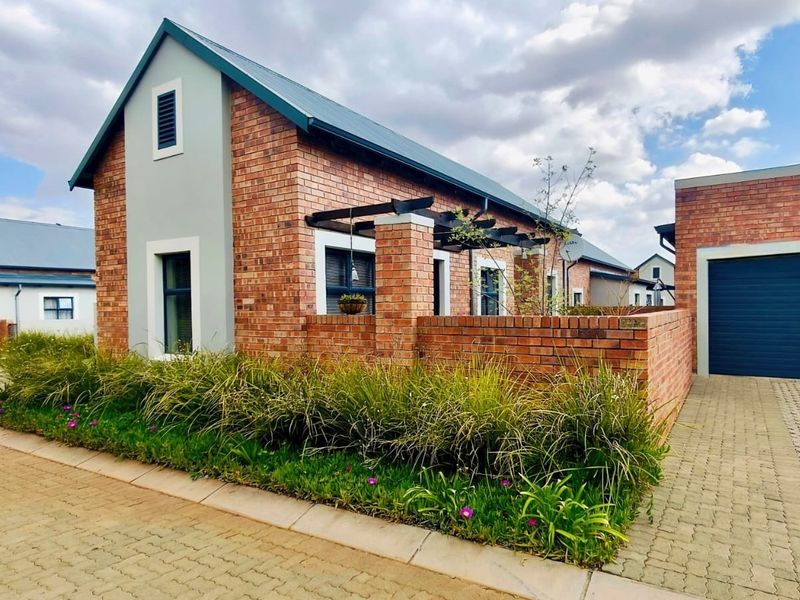 A well-maintained townhouse exterior featuring face brick construction, a pitched metal roof, a paved driveway, and an integrated garage.