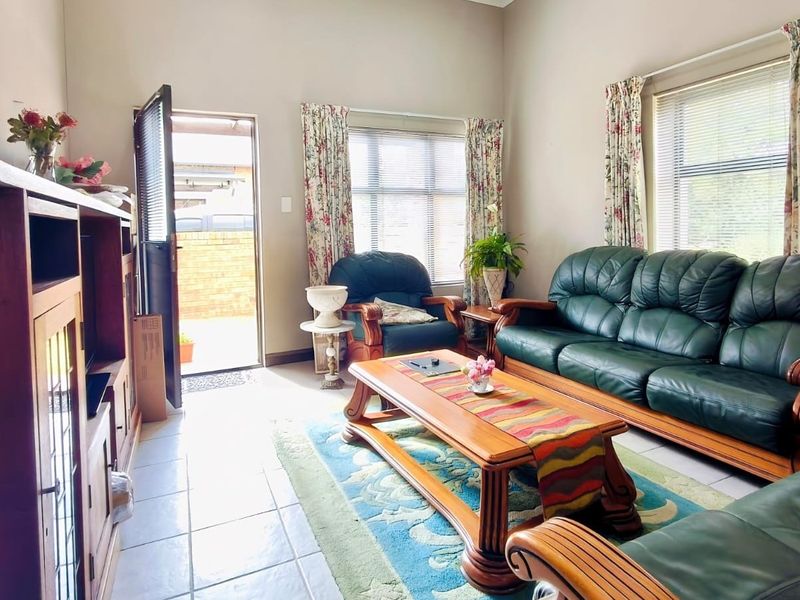 A bright living room featuring tiled flooring, large windows with venetian blinds, and direct access to an outdoor area.