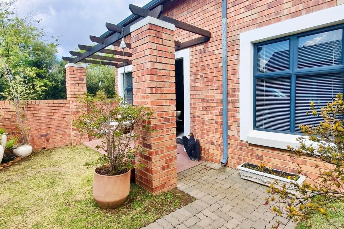 A rear exterior view of a townhouse featuring a brick facade, a covered patio area with a pergola, and a small private garden.