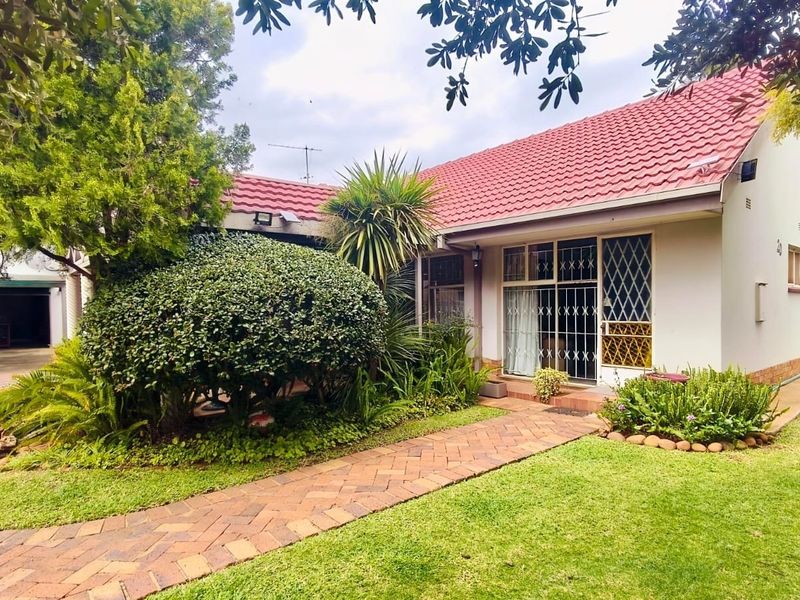 Front view of a well-maintained house featuring a red tiled roof, brick paved walkway, and established garden landscaping.