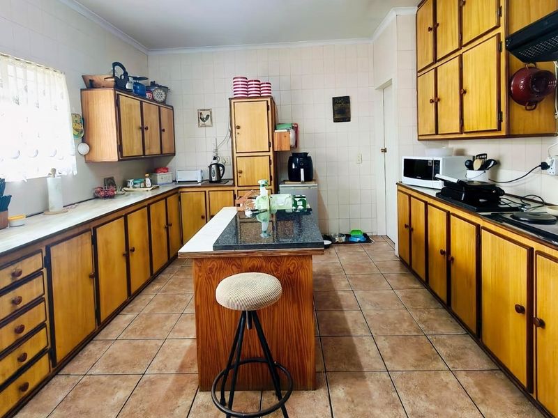 A functional kitchen featuring extensive wooden cabinetry, a central island, ceramic tiling, and built-in cooking appliances, offering a classic layout with potential for modernization.