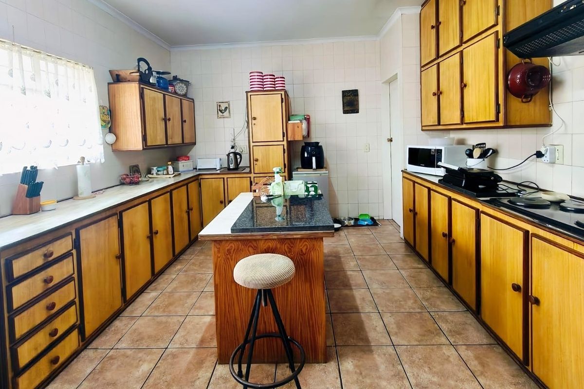 A functional kitchen featuring extensive wooden cabinetry, a central island, ceramic tiling, and built-in cooking appliances, offering a classic layout with potential for modernization.