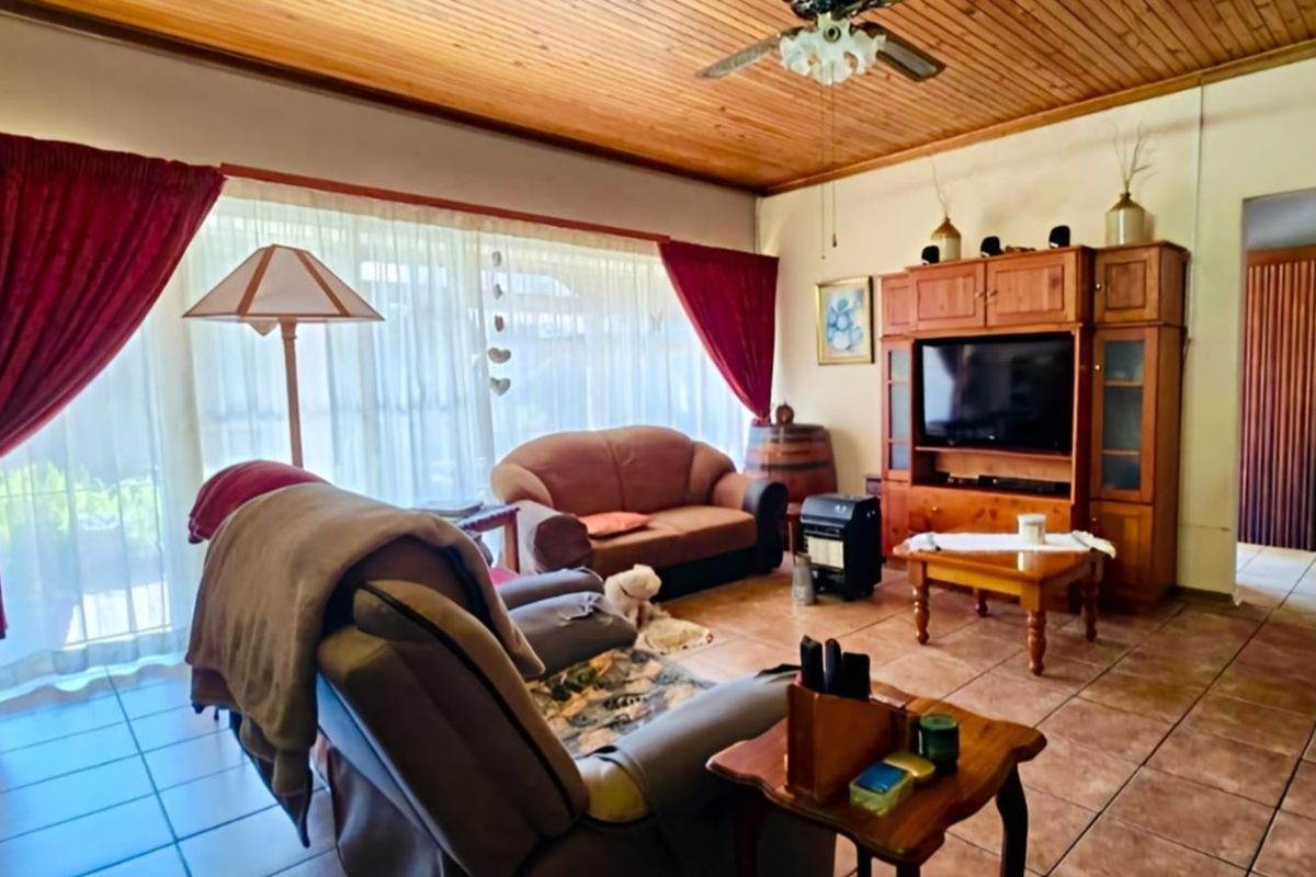A living room featuring a warm timber-paneled ceiling, ceiling fan, and tiled flooring, with large sliding glass doors providing natural light.