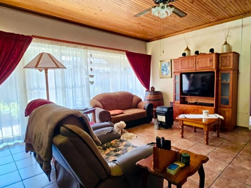 A living room featuring a warm timber-paneled ceiling, ceiling fan, and tiled flooring, with large sliding glass doors providing natural light.