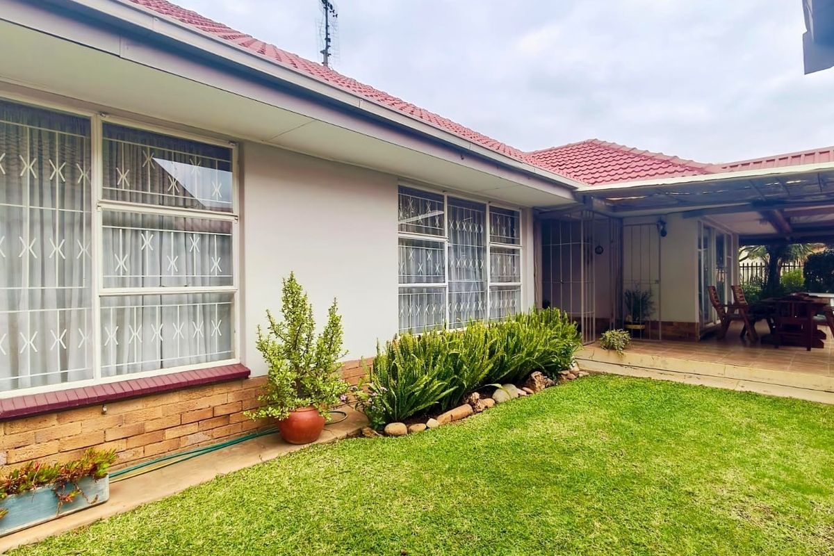 Rear view of the house featuring a tiled roof, brick exterior, security bars on windows, and a covered patio area overlooking the garden.