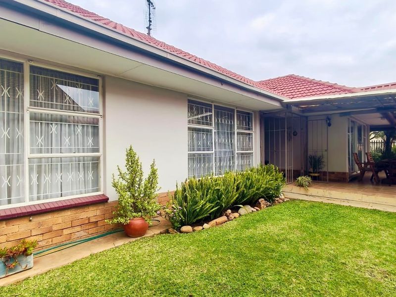 Rear view of the house featuring a tiled roof, brick exterior, security bars on windows, and a covered patio area overlooking the garden.
