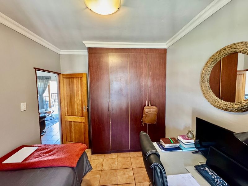 A bedroom featuring built-in wooden cupboards, tiled flooring, and crown molding, with an adjacent doorway leading to another living space.