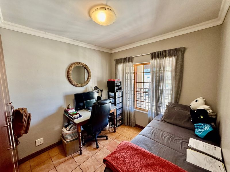 A functional bedroom featuring tiled flooring, cove cornicing, and a window fitted with security bars, providing a practical living or workspace.