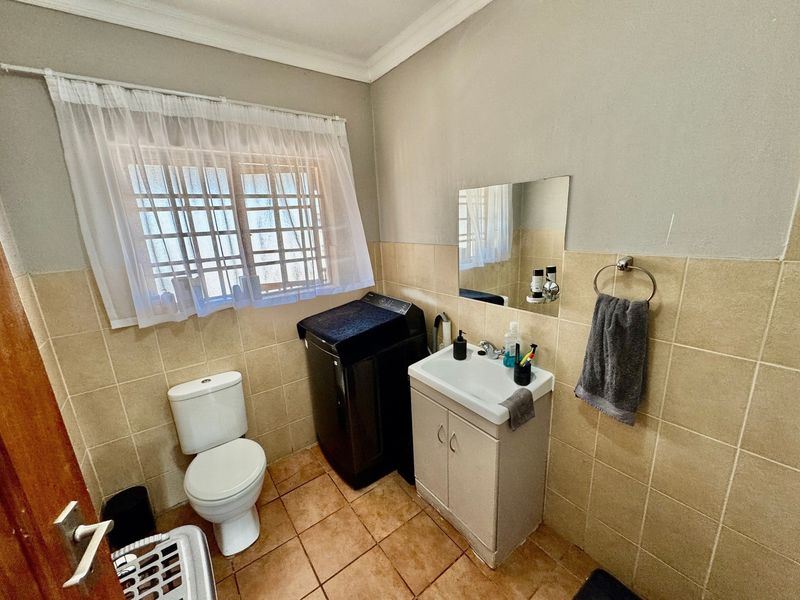 A functional bathroom featuring a toilet, vanity cabinet with washbasin, and tiled finishes, including security bars on the window.