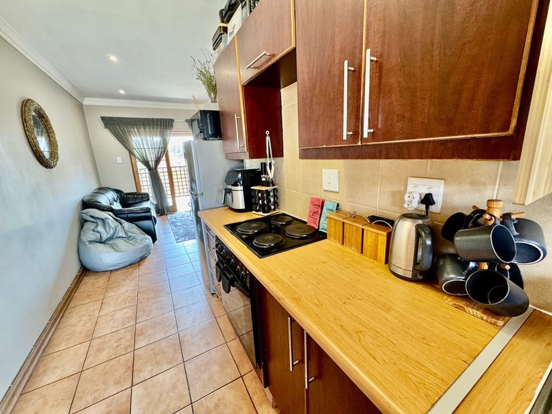 Open-plan kitchen and living area featuring wood-finish cabinetry, electric hob, oven, and tiled flooring, leading to a balcony area.