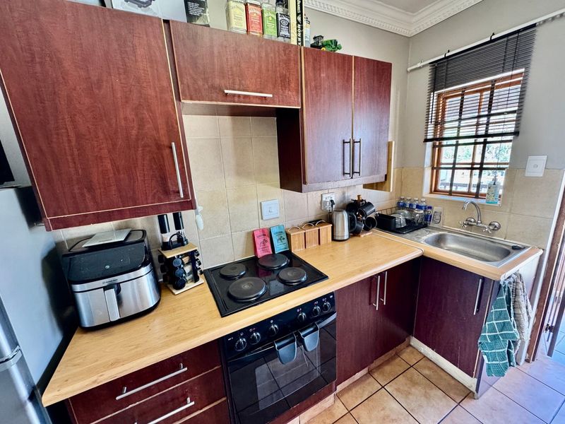 Compact kitchen featuring dark wood-finish cabinetry, laminate countertops, a built-in electric oven and hob, and a stainless steel sink with tiled backsplash.