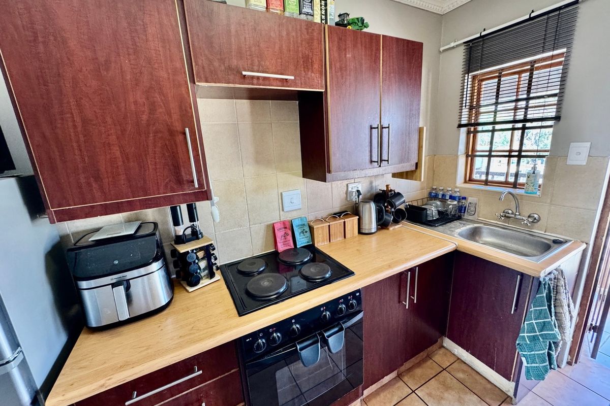 Compact kitchen featuring dark wood-finish cabinetry, laminate countertops, a built-in electric oven and hob, and a stainless steel sink with tiled backsplash.
