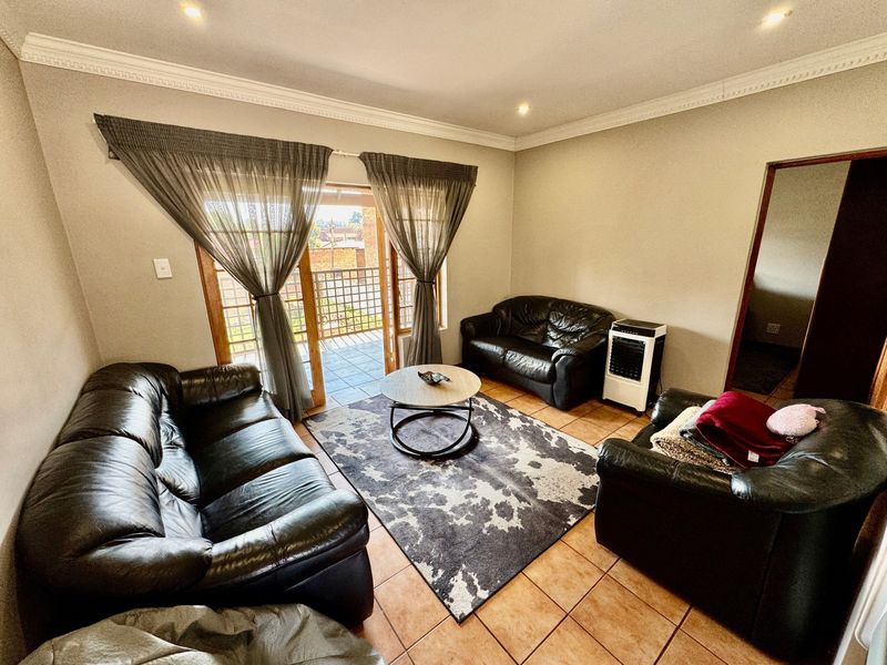 A living room featuring tiled flooring, crown molding, and a sliding glass door providing access to an outdoor balcony area.