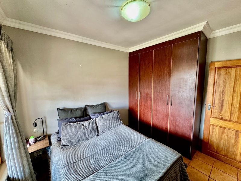 A bedroom featuring built-in wooden wardrobes, tiled flooring, and classic ceiling cornicing, providing a functional and well-defined sleeping space.