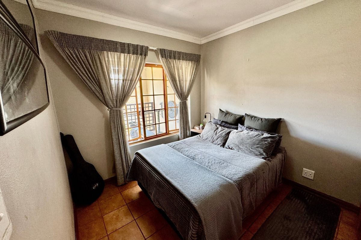 A cozy bedroom featuring tiled flooring, crown molding, and a window fitted with security bars, providing a functional and comfortable living space.