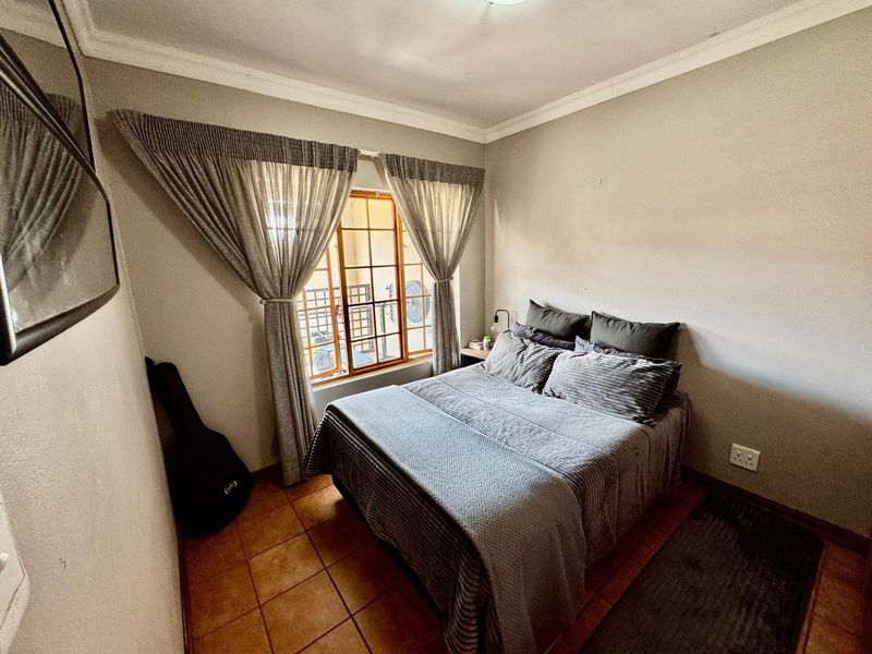 A cozy bedroom featuring tiled flooring, crown molding, and a window fitted with security bars, providing a functional and comfortable living space.