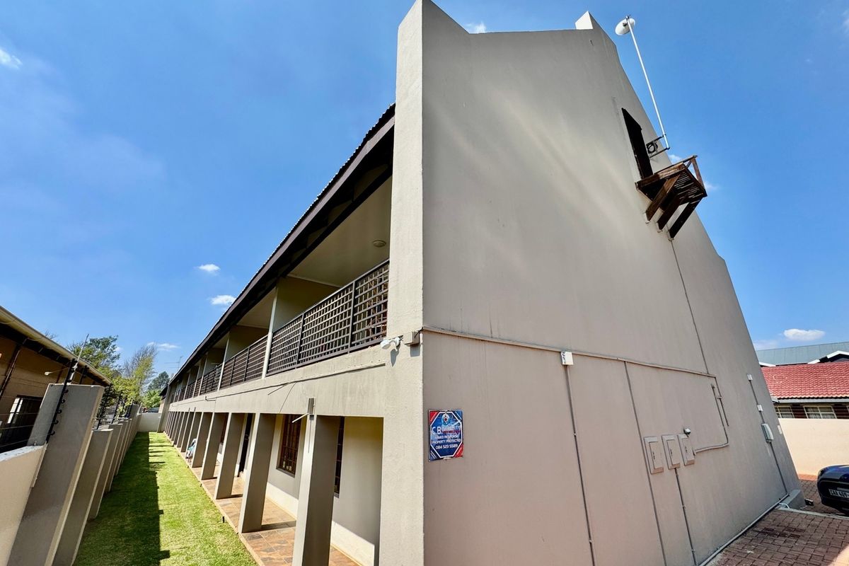 Rear view of the apartment building featuring a long balcony with metal balustrades, paved ground level walkway, and well-maintained exterior walls.