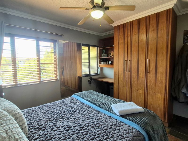 A bedroom featuring extensive built-in wooden cabinetry, a dedicated desk area, ceiling fan, and venetian blinds, offering functional storage and workspace.