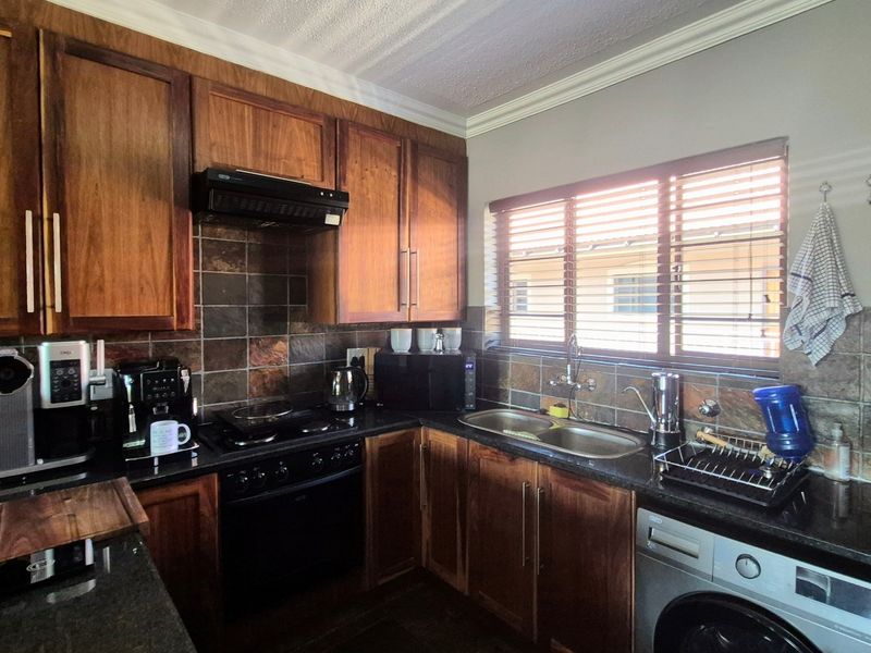 A functional kitchen featuring wooden cabinetry, granite countertops, a double bowl sink, and built-in cooking appliances with a tiled backsplash.