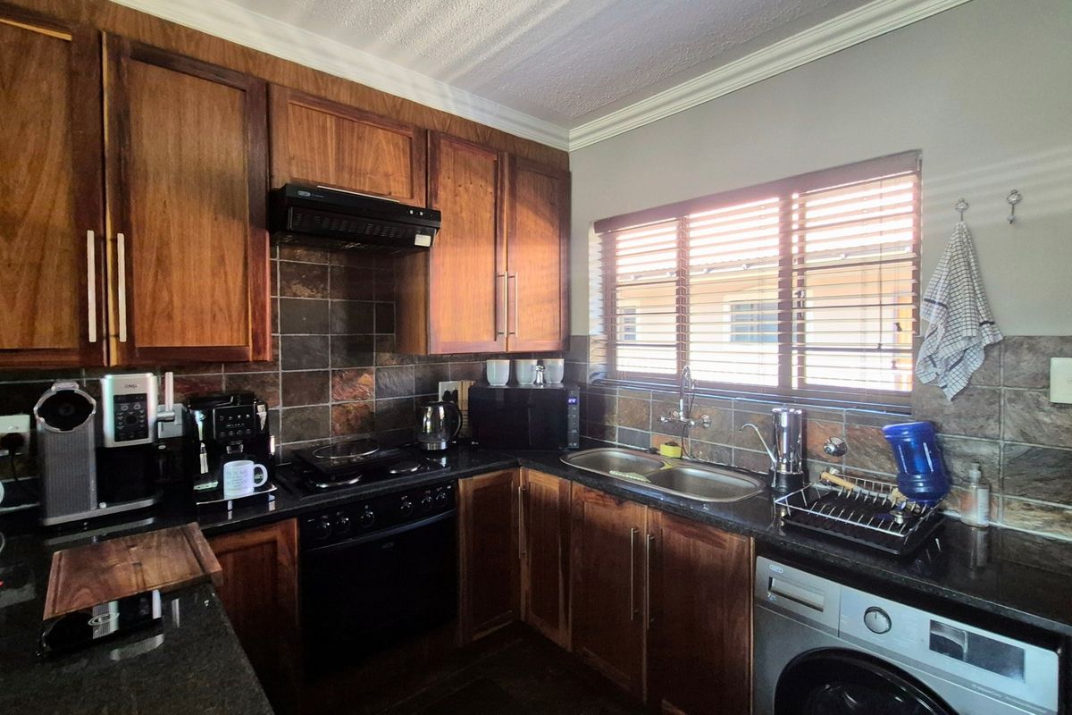 A functional kitchen featuring wooden cabinetry, granite countertops, a double bowl sink, and built-in cooking appliances with a tiled backsplash.