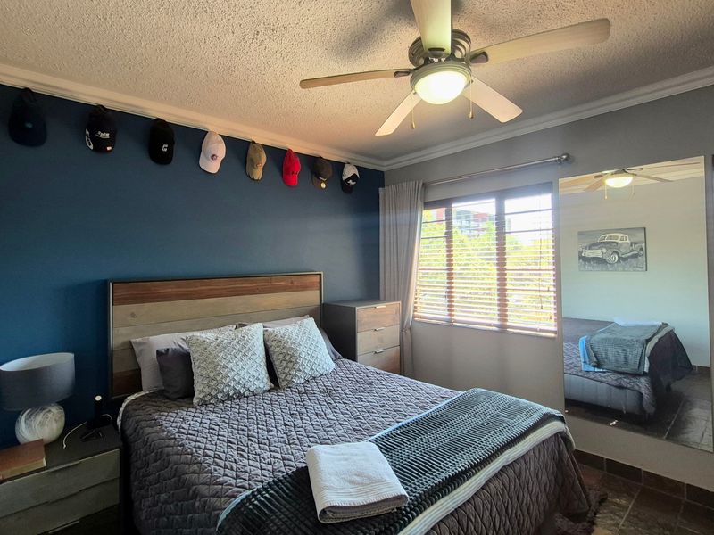A well-lit bedroom featuring a ceiling fan, tiled flooring, and a large wall-mounted mirror, providing a comfortable and functional living space.