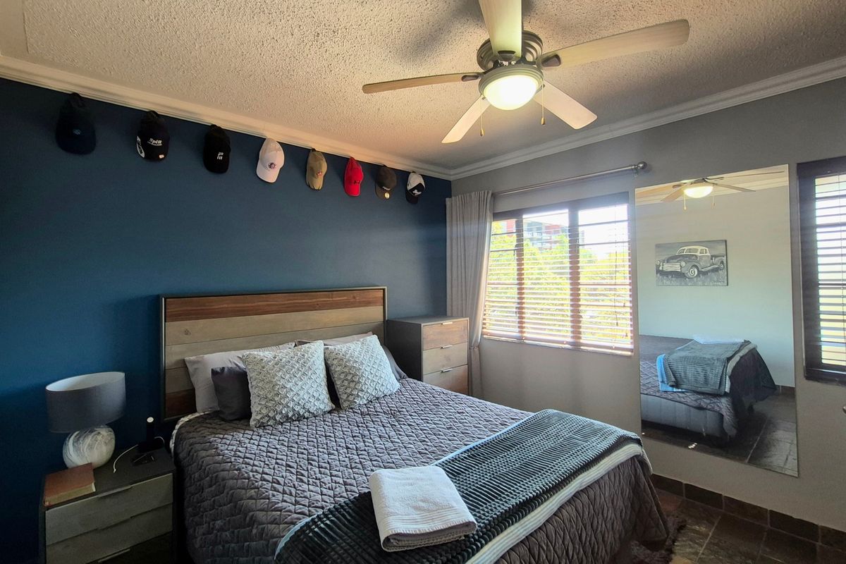 A well-lit bedroom featuring a ceiling fan, tiled flooring, and a large wall-mounted mirror, providing a comfortable and functional living space.