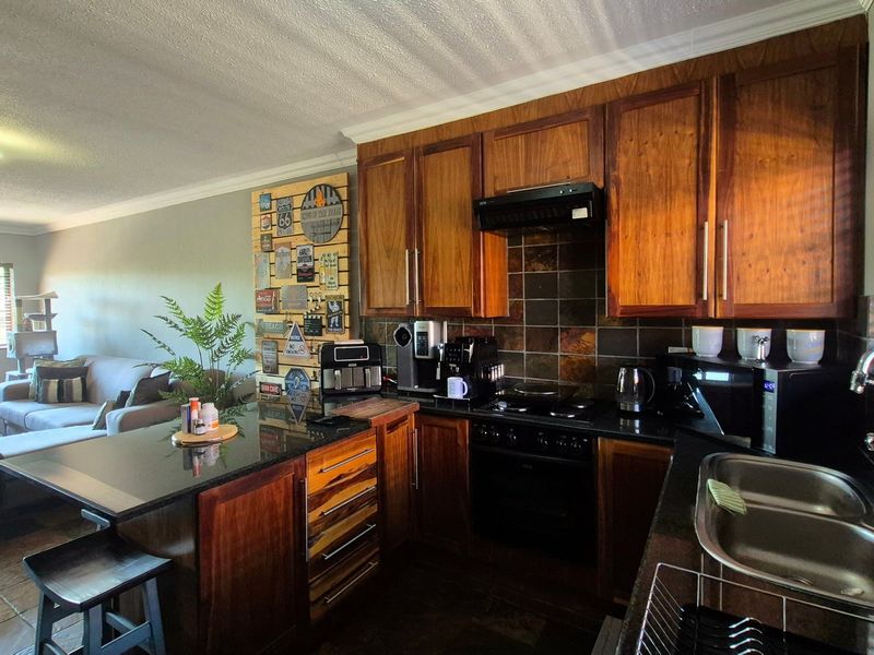 Open-plan kitchen and living area featuring wooden cabinetry, granite countertops, built-in oven, and tiled flooring, creating a functional and connected living space.