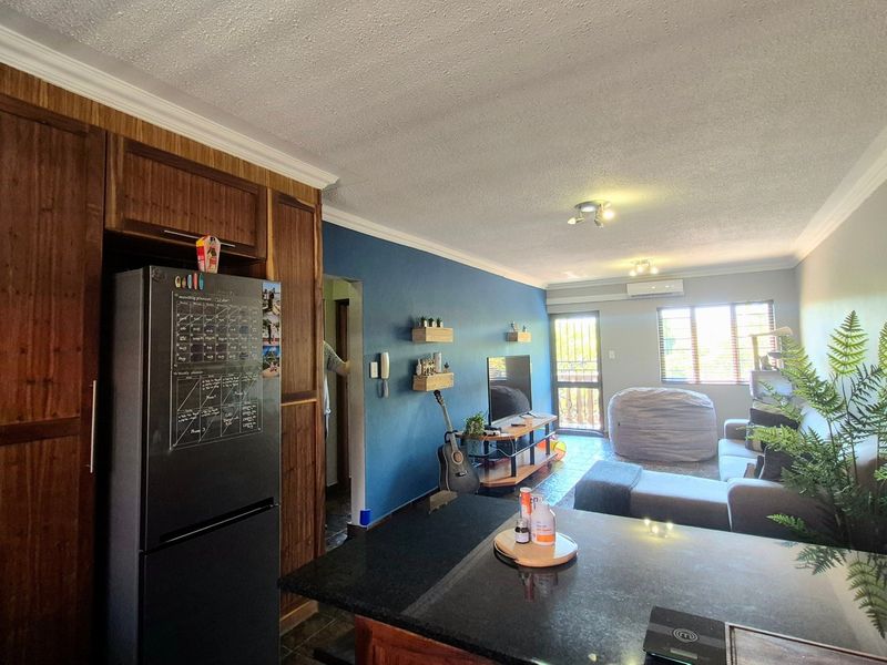 Open-plan living area featuring a kitchen with dark cabinetry and granite countertops, flowing into a comfortable lounge space with air conditioning.