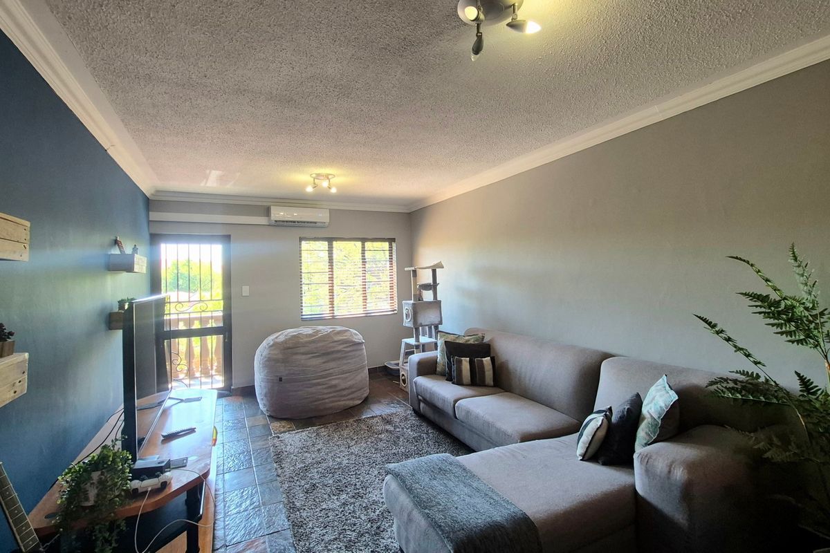 A living room featuring tiled flooring, a split-system air conditioner, and access to an outdoor area through a security gate.