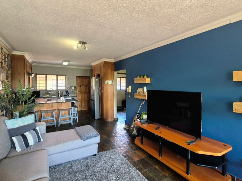 Open-plan living and kitchen area featuring dark tiled flooring, a blue accent wall, and wooden kitchen cabinetry.