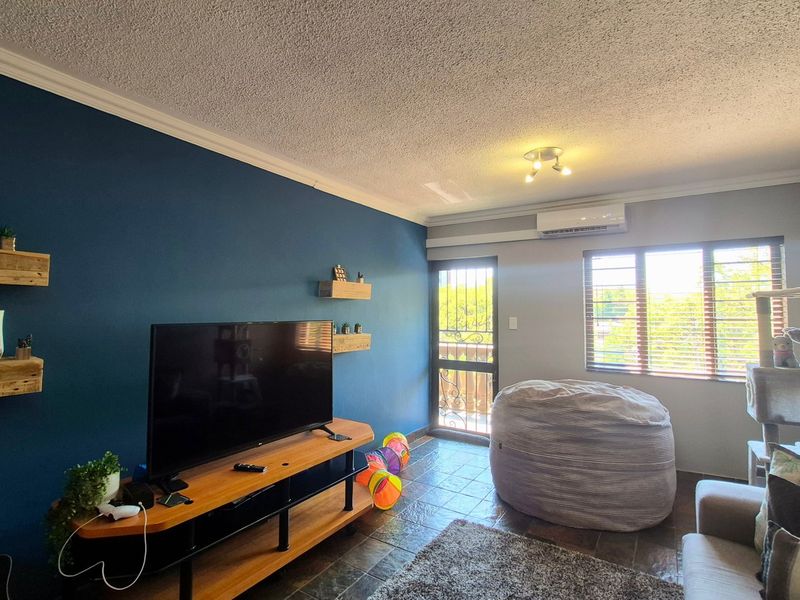 A living room featuring tiled flooring, an air conditioning unit, and a security gate leading to an outdoor area.