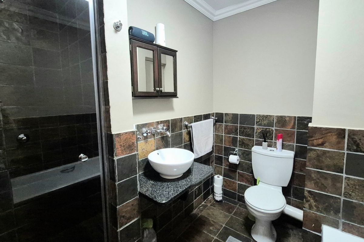 A bathroom featuring a vessel sink on a granite vanity, a toilet, and a shower enclosure with dark slate tiling throughout.