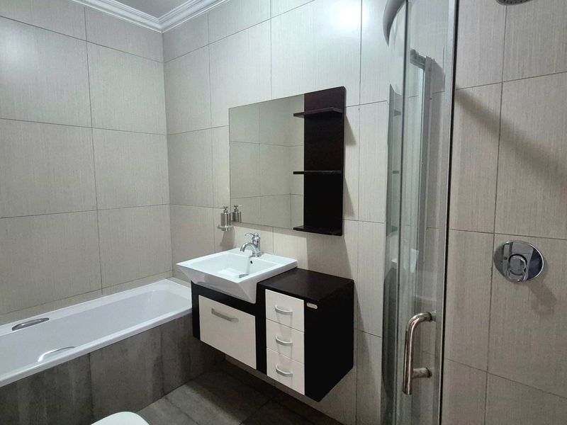 Modern bathroom featuring a built-in vanity, wall-mounted mirror, bathtub, and a separate glass-enclosed shower with neutral ceramic tiling.