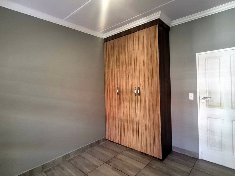 A clean, empty bedroom featuring modern wood-finish built-in wardrobes, neutral grey walls, and tiled flooring with crown molding detail.