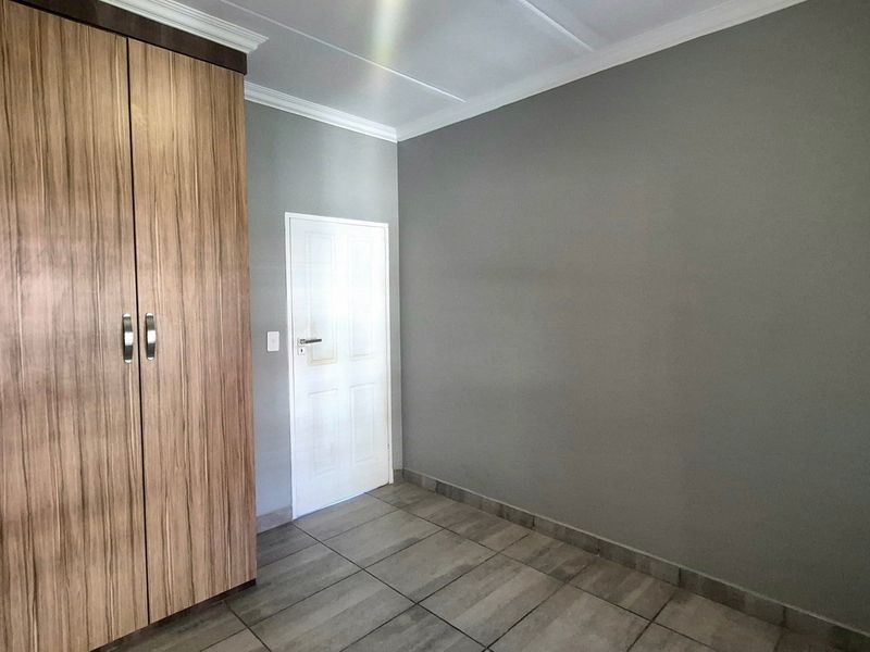 A clean, empty bedroom featuring modern tiled flooring, a large built-in wooden wardrobe, and neutral grey walls with coved ceiling detailing.