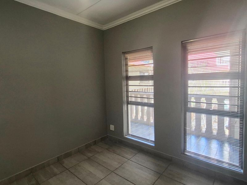 A clean, empty bedroom featuring neutral grey walls, tiled flooring, and two windows fitted with venetian blinds.