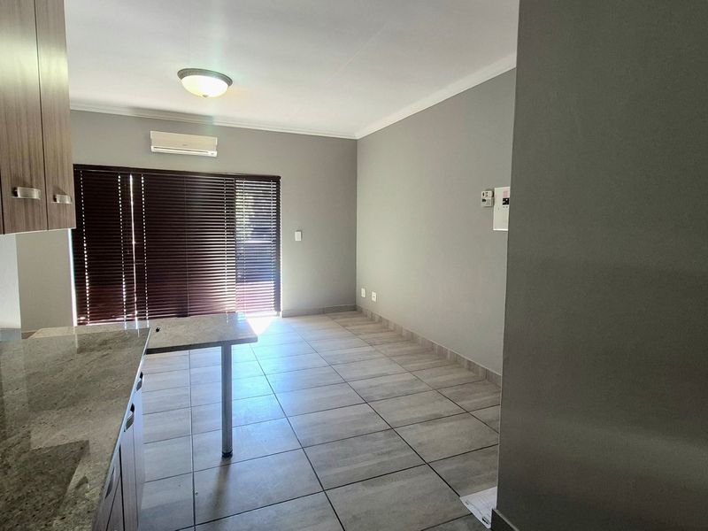 An open-plan living and kitchen area featuring tiled flooring, granite countertops, built-in cabinetry, and a wall-mounted air conditioning unit.