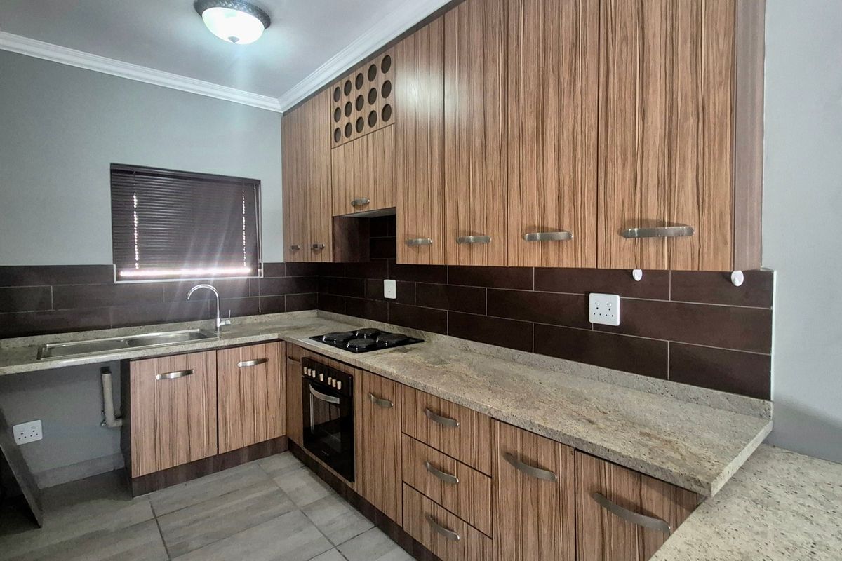 A modern kitchen featuring wood-grain cabinetry, granite countertops, a built-in oven, gas hob, and a tiled backsplash.