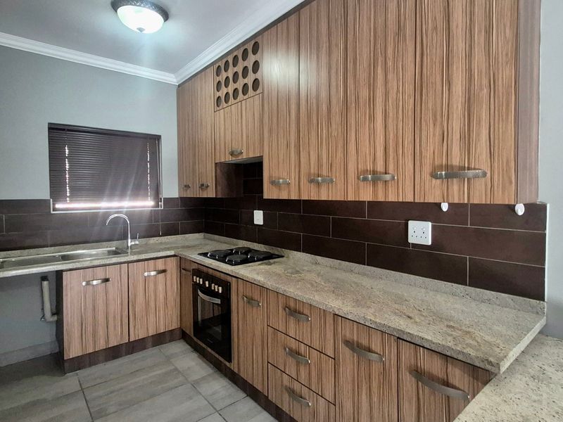 A modern kitchen featuring wood-grain cabinetry, granite countertops, a built-in oven, gas hob, and a tiled backsplash.