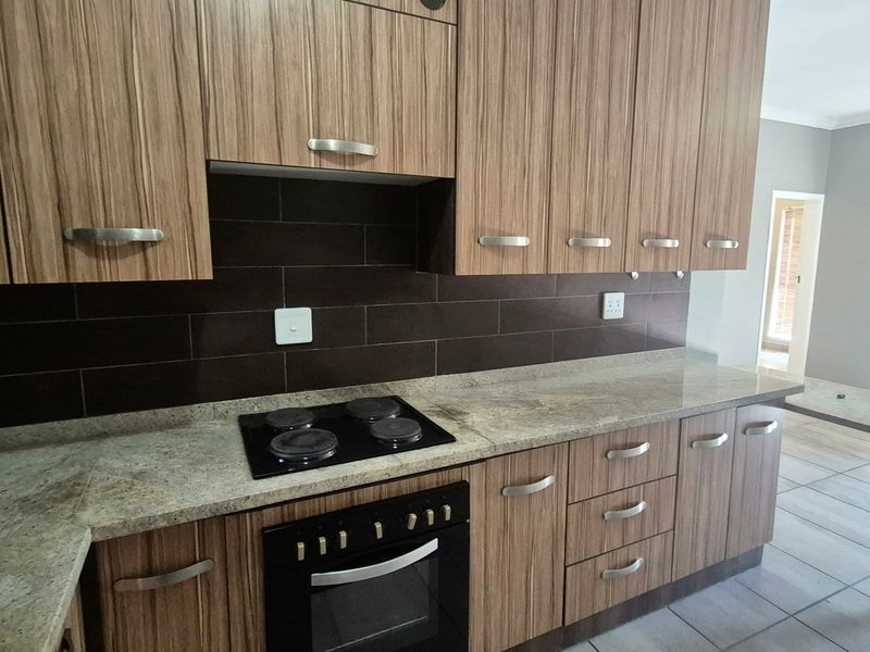 Modern kitchen featuring wood-grain cabinetry, stone countertops, a built-in electric oven and hob, and a dark tiled backsplash.