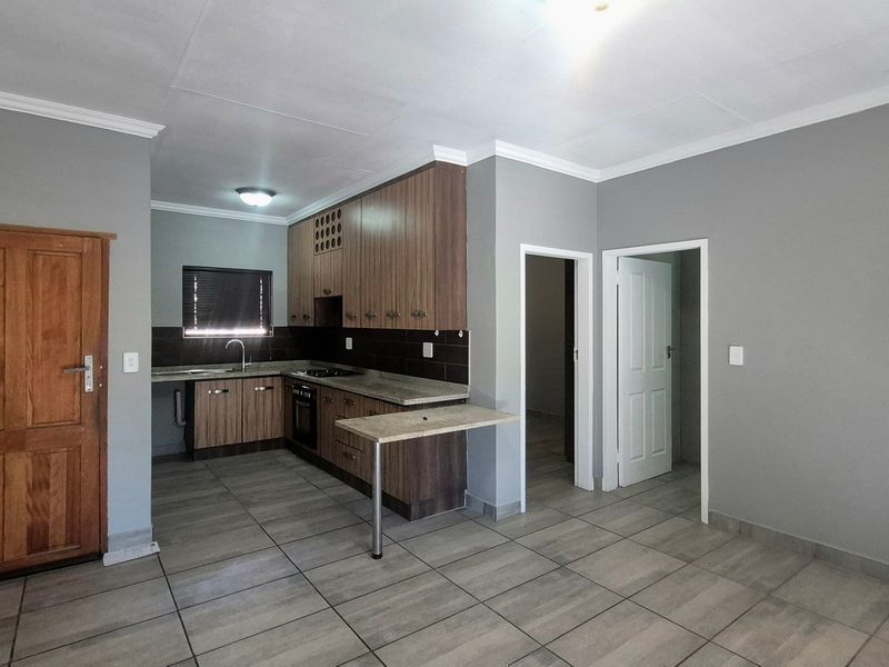 An open-plan kitchen area featuring modern cabinetry, built-in appliances, tiled flooring, and neutral grey walls, providing a clean and functional living space.