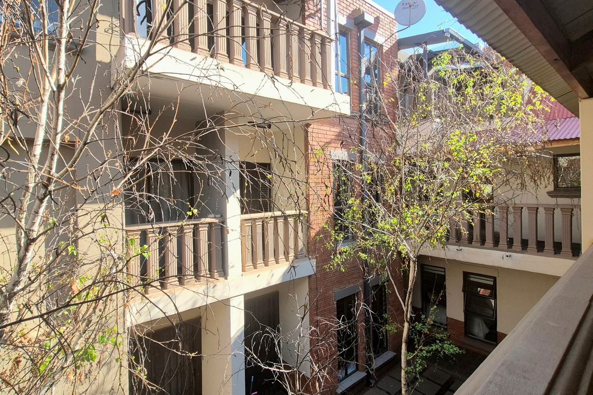 View of the apartment building exterior featuring brick facade, multiple balconies with balustrades, and surrounding trees.
