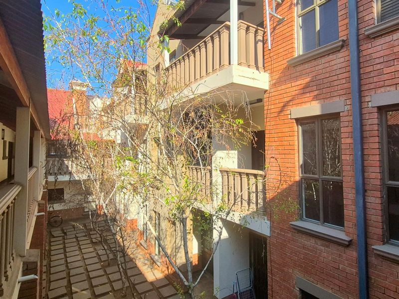 View of the apartment complex rear courtyard featuring brick facade, multiple balconies with railings, and a paved ground level area.